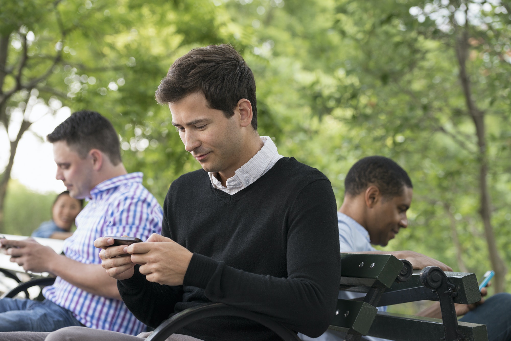 People sitting in the park, each on their own phone or using a tablet.