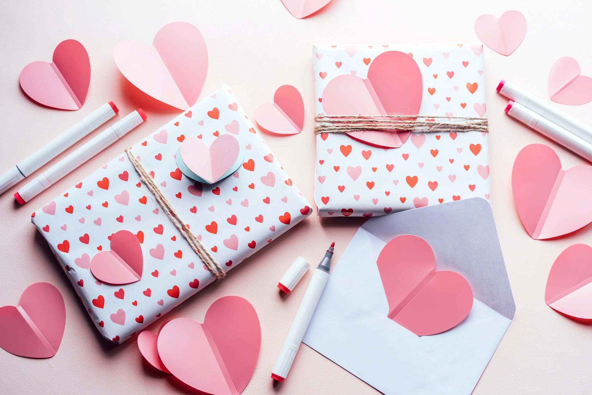 Top view of wrapped gifts and handmade hearts on a pink background.