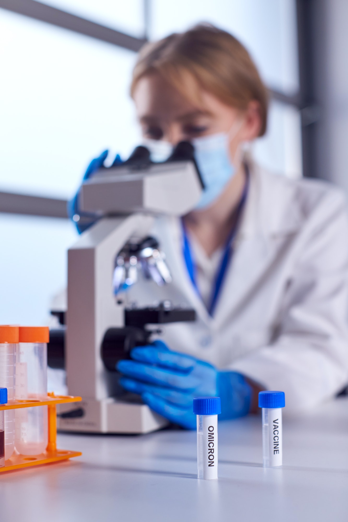 Female Lab Worker Wearing PPE Researching Covid-19 Omicron Variant And Vaccine With Microscope