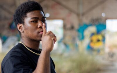 Portrait of a young black boy ordering to be quiet. Graffiti wall background.