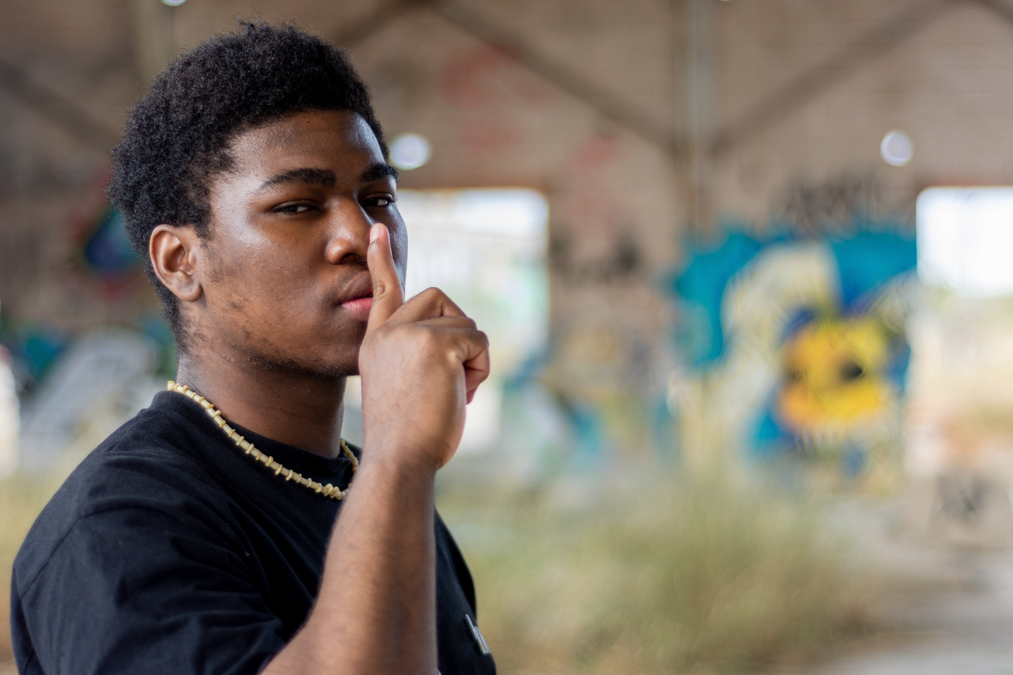 Portrait of a young black boy ordering to be quiet. Graffiti wall background.