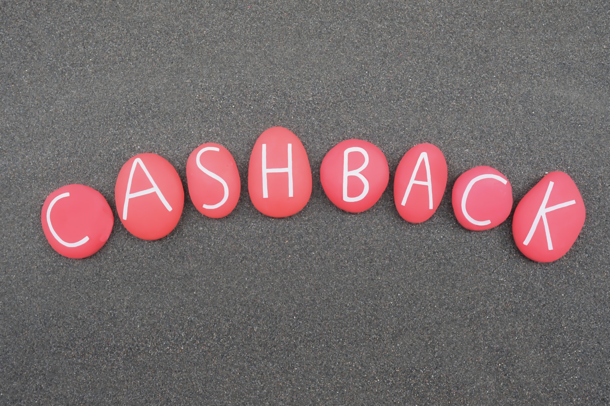 Cashback, reward program word composed with red colored stone letters over black sand