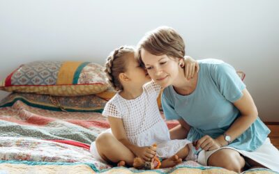 Mother and her small daughter are talking on the bed. The girl says something on moms ear