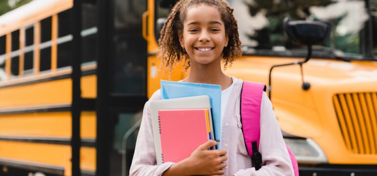 Smiling african-american schoolgirl going back to school with books and copybooks