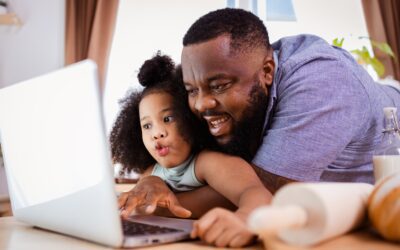 African American Dad teaches his little girl to make cookies by watching how to do it on laptop