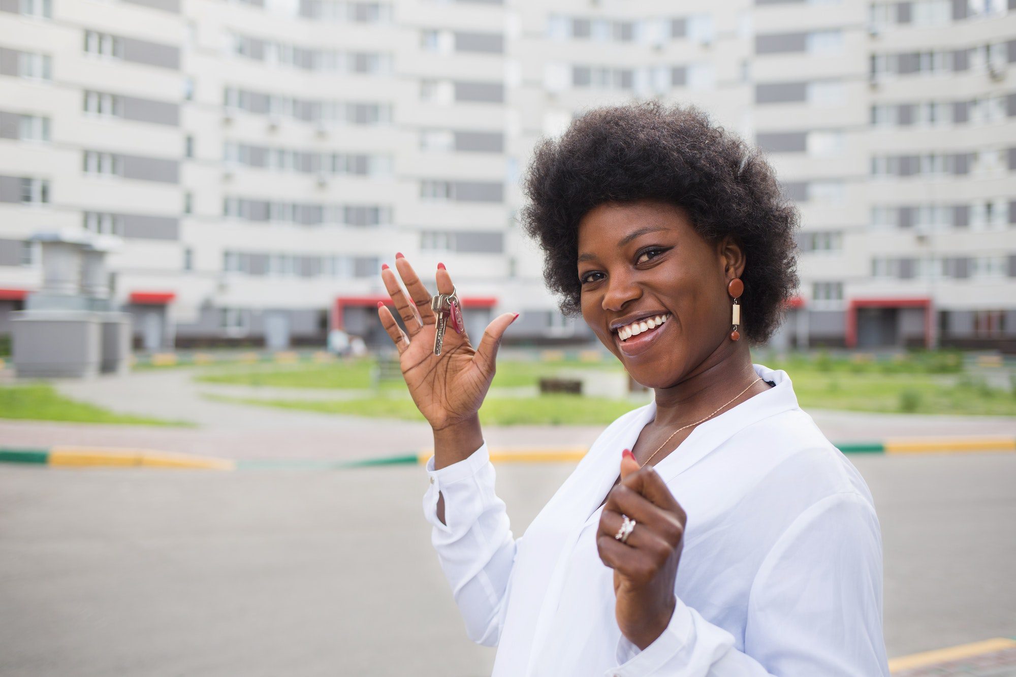 black girl with keys to apartment on background of multi-storey building. home buying and moving