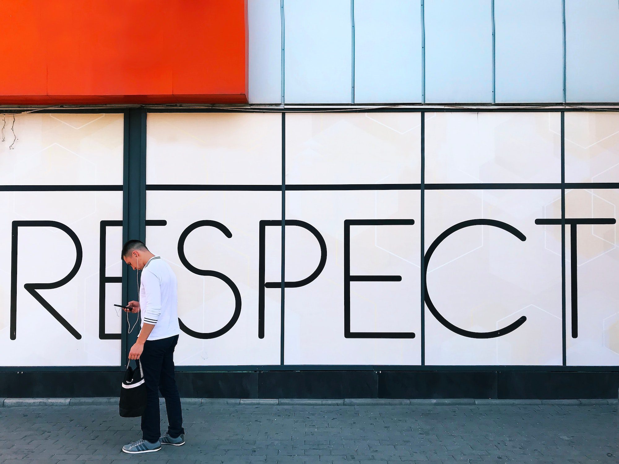 Young man using mobile phone in front of a word “respect” on wall