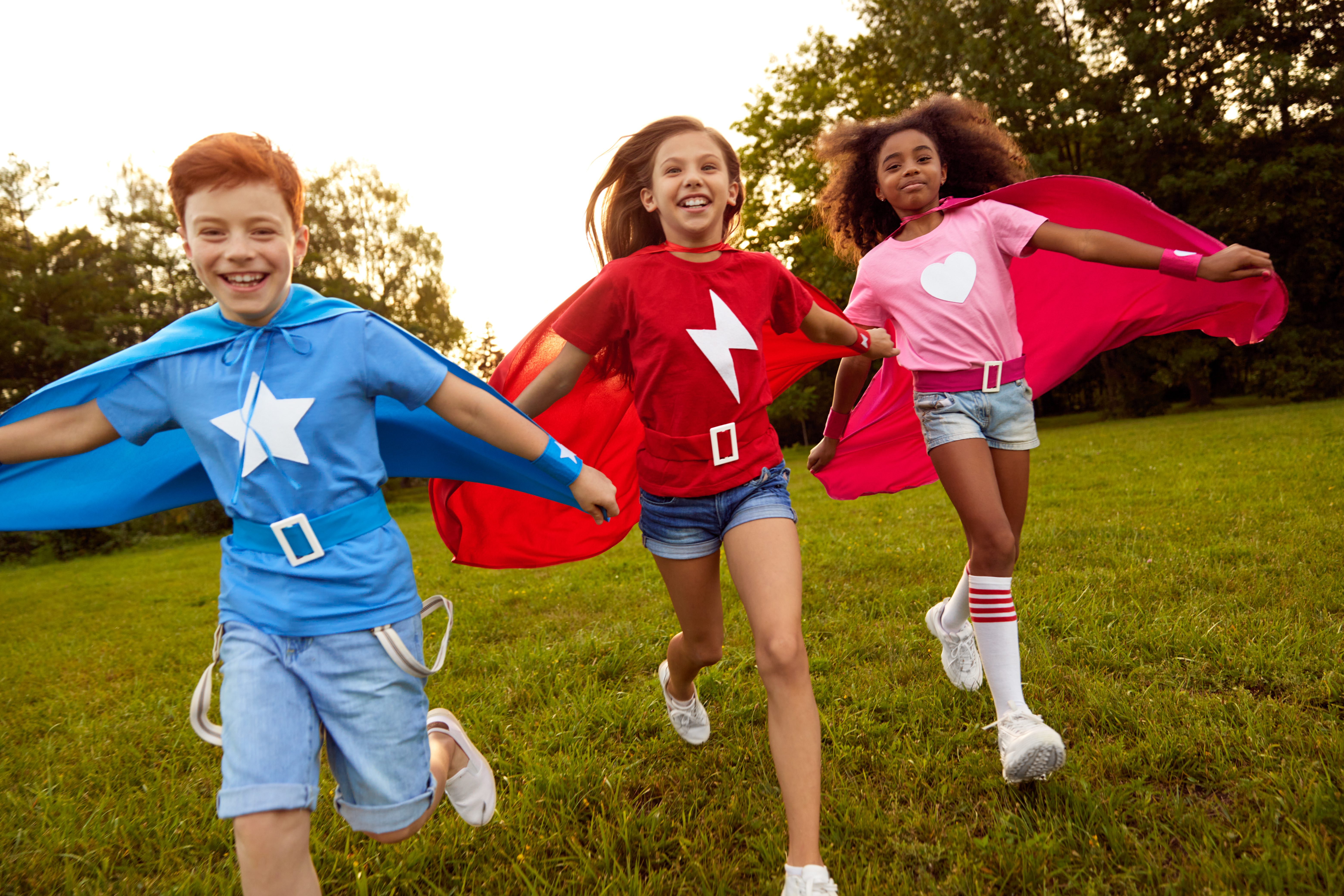 Carefree diverse superhero children running along meadow