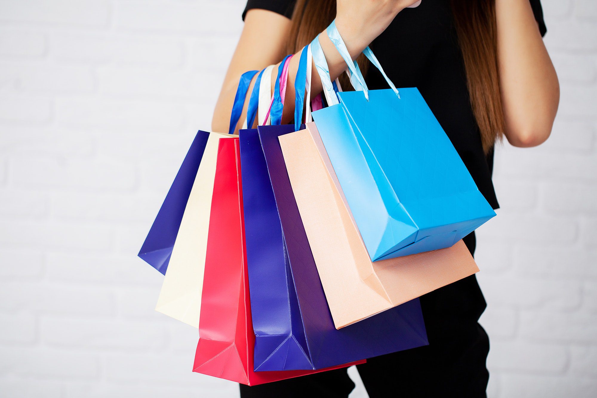 Shopping. Closeup of woman holding color paper shopping bag on white wall background Shopping. Closeup of woman holding color paper shopping bag on white wall background