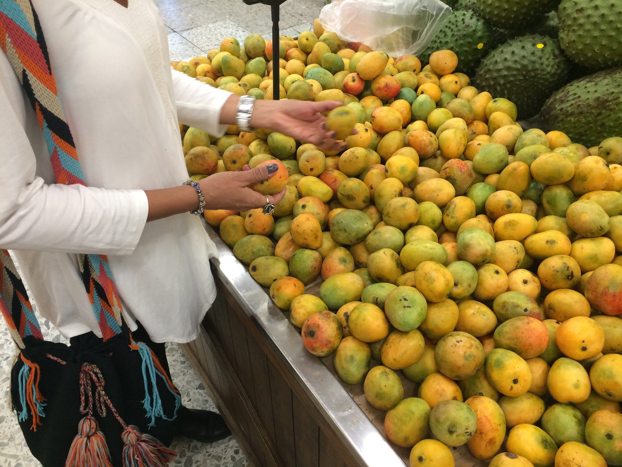 Woman picking & choosing fresh & exotic fruits like guanábana at the grocery store.