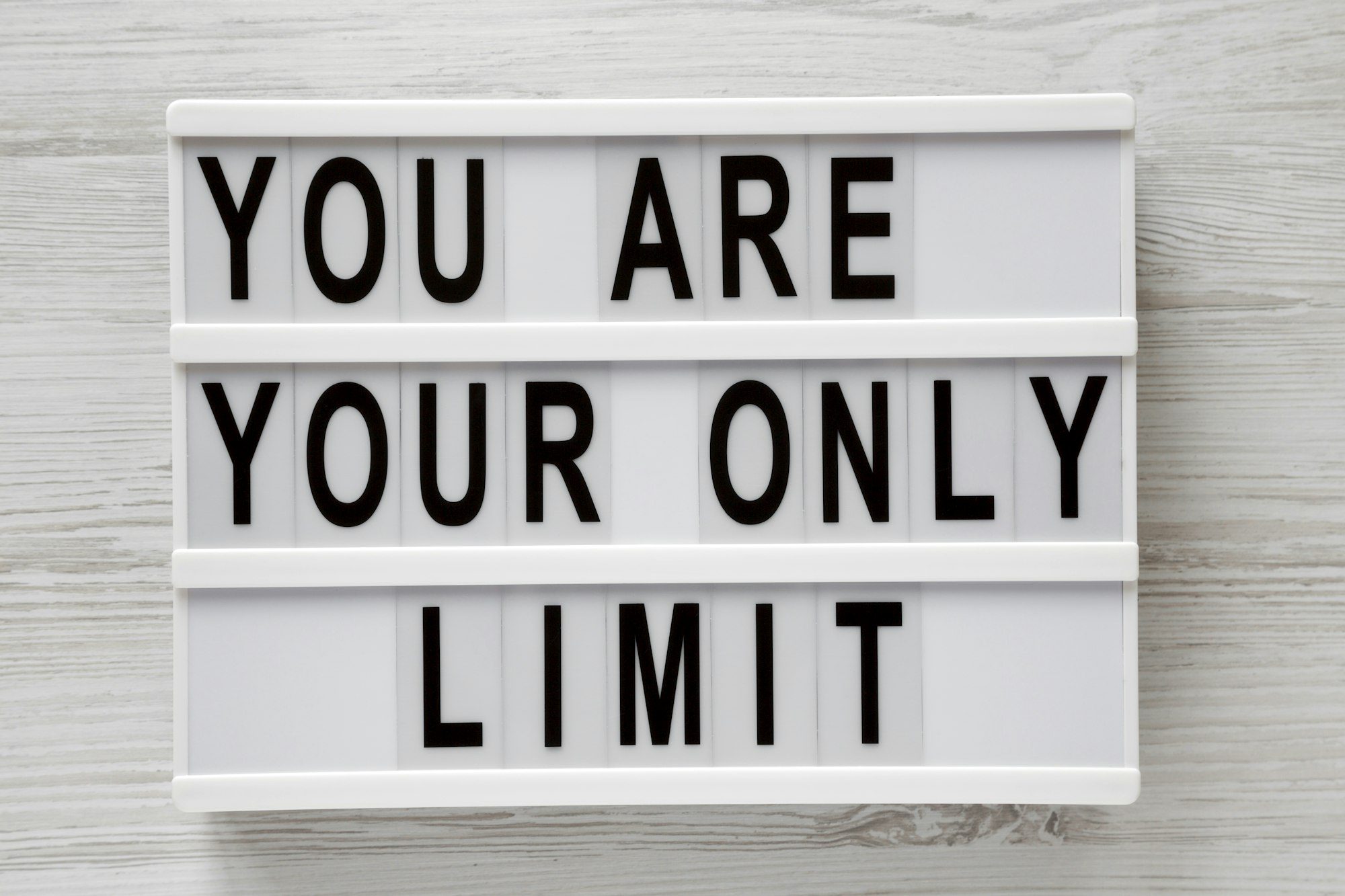 'You are your only limit' words on a lightbox over white wooden background, top view.