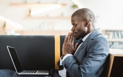 smiling african american businessman with closed eyes praying with laptop