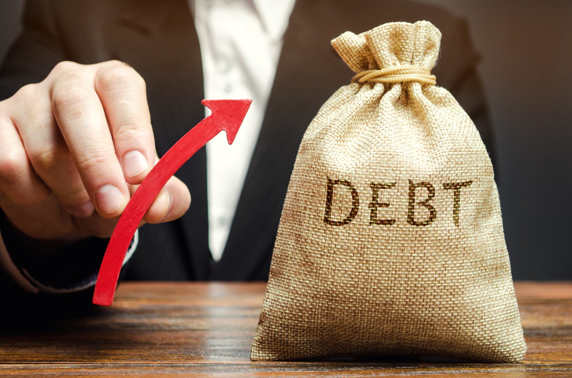 A bag with the word Debt and an up arrow in the hands of a businessman