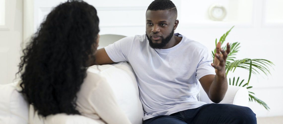 Angry man blaming his girlfriend sitting at sofa at home