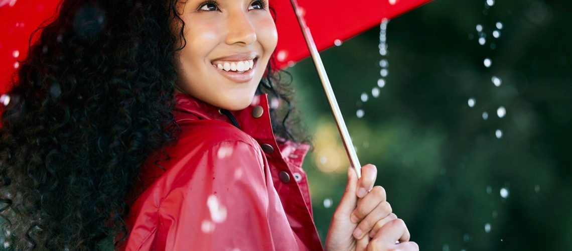 Its raining, its pouring. Shot of a beautiful young woman standing in the rain with an umbrella.