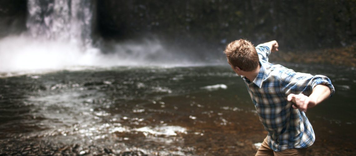 Man Throwing Stone At Waterfall