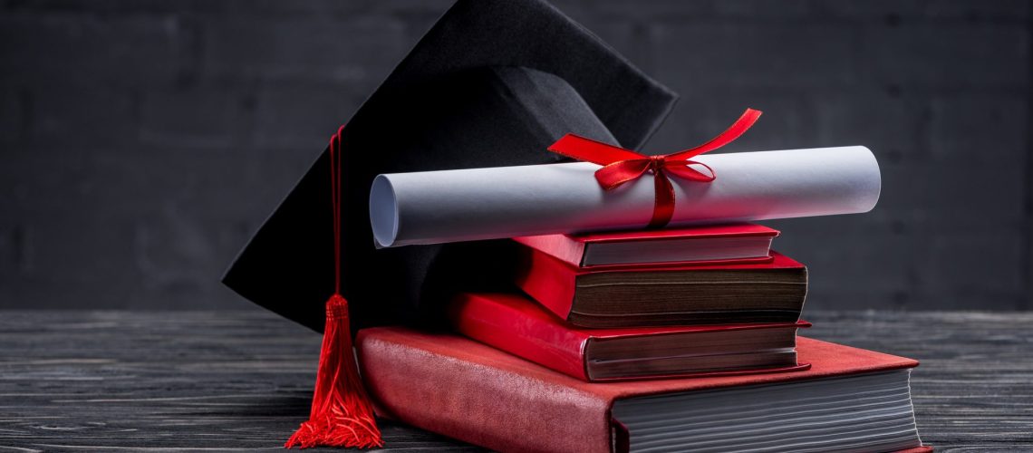 Stack of books with diploma and graduation hat on table