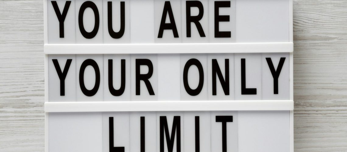 'You are your only limit' words on a lightbox over white wooden background, top view.